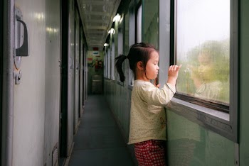 Photo of Girl Standing by Window in Train Hallway Looking Outside While Taking a Photo