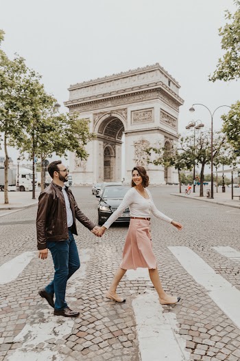 Photo of Happy Couple Holding Hands While Crossing the Street with The Arc de Triomphe in the Background