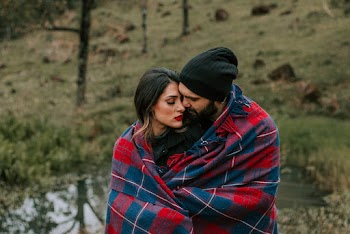 Photo of Hugging Couple Covered in Red and Black Blanket Outdoors
