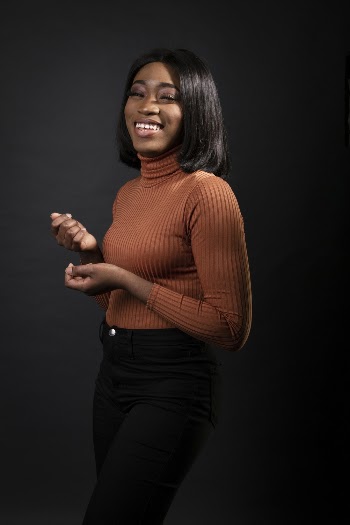Photo of Laughing Woman in Brown Turtleneck Sweater and Black Pants Posing In Front of Black Background