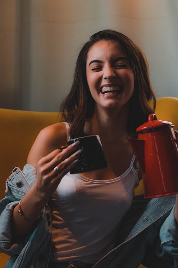 Photo of Laughing Woman While Holding Mug and Kettle