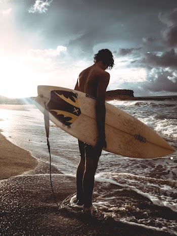 Photo of Man Carrying Surfboard While Standing on the Beach