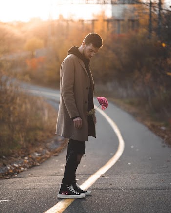 Photo of Man Holding Flower While Standing in the Middle of an Empty Road 