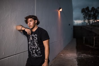 Photo of Man in a Black T-shirt Leaning on Gray Wall Looking Into the Distance