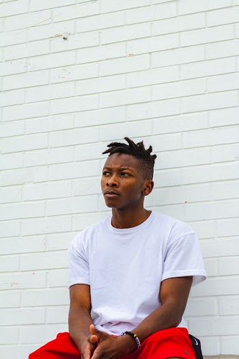 Photo of Man in a White T-shirt and Red Pants Sitting In Front of White Wall Looking Away