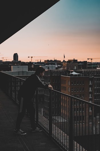 Photo of Man in Black and White Tracksuit Leaning on Balcony Railings
