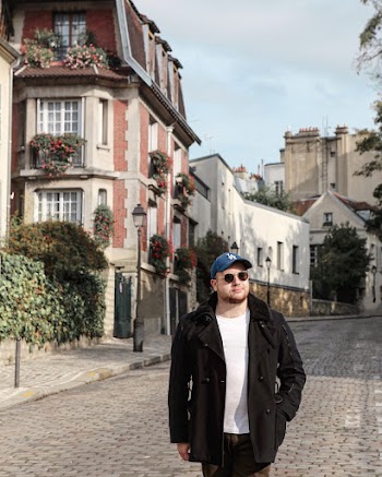 Photo of Man in Black Coat Standing Alone on Paved Street with Houses in the Background