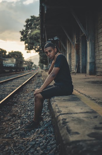 Photo of Man in Black T-shirt and Shorts Sitting on Train Platform Posing