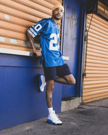 Photo of Man in Blue American Football Jersey and Blue Shorts Leaning on Closed Store Posing