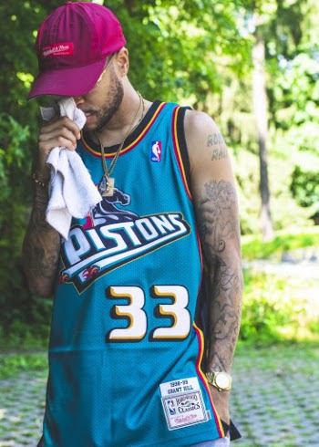 Photo of Man in Blue Pistons Basketball Jersey and Maroon Hat Posing While Looking Down