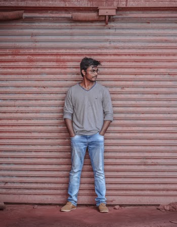 Photo of Man in Gray Long-sleeved T-shirt and Blue Jeans Posing In Front of Roll Up Door Looking Away