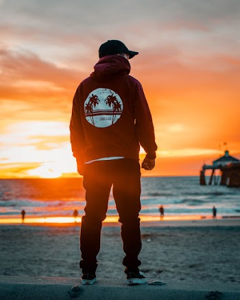 Photo of Man in Hoodie and Cap Standing at the Shore During Golden Hour