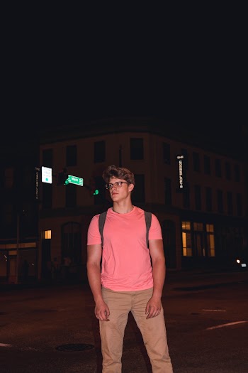 Photo of Man in Pink Shirt Standing in  the Middle of a Road at Nighttime Posing While Looking Away