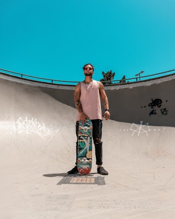 Photo of Man in Pink Tank Top and Black Jeans Posing With a Skateboard