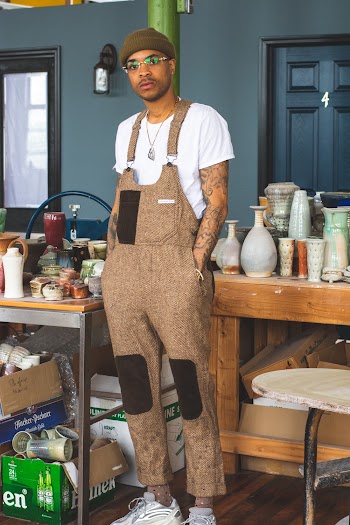 Photo of Man In Tweed Dungarees Standing Near Tables Posing With Hands in His Pockets