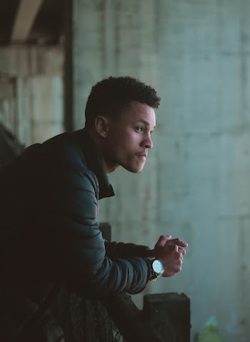 Photo of Man Leaning on Metal Railing Looking into The Distance