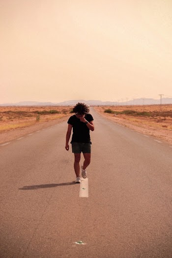Photo of Man Looking Down While Walking in the Middle of the Road
