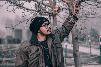 Photo of Man Looking Up While Holding a Tree Branch