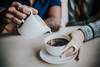 photo of man pouring milk on coffee