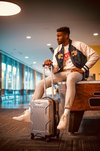 Photo of Man Sitting on a Pool Table While Holding His Luggage Posing
