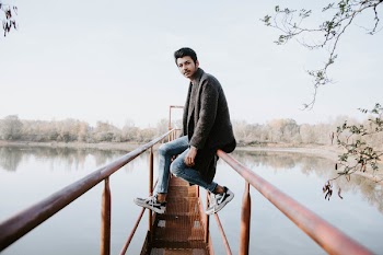 Photo of Man Sitting on Brown Metal Bridge Railing
