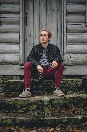 Photo of Man Sitting on Concrete Stair Near Wooden Shed Holding Camera