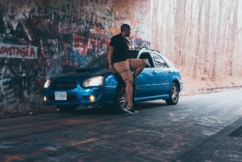 Photo of Man Sitting on Hood Of Parked Blue 5-door Subaru Hatchback