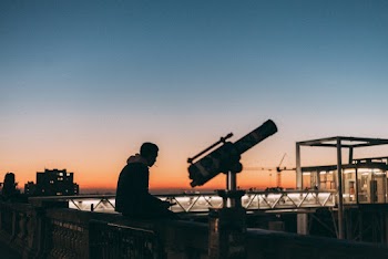 Photo of Man Sitting on Ledge Near Telescope