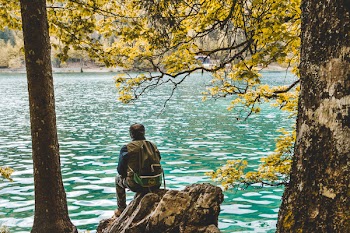 Photo of Man Sitting on Rock Near Lake