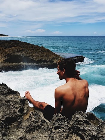Photo of Man Sitting on Rock Near Sea