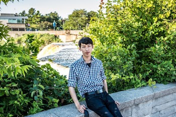 Photo of Man Sitting on Stone Railing Near Green Plants With Waterfall in the Background