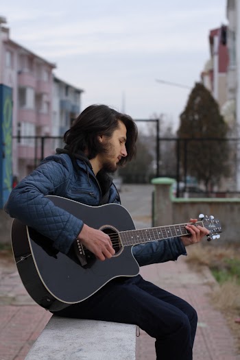 Photo of Man Sitting While Playing Acoustic Guitar