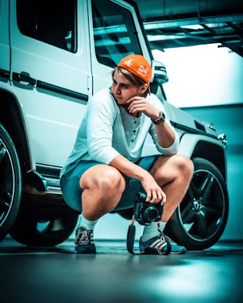 Photo of Man Squat Posing Beside White Mercedes G Wagon While Holding a Dslr Camera