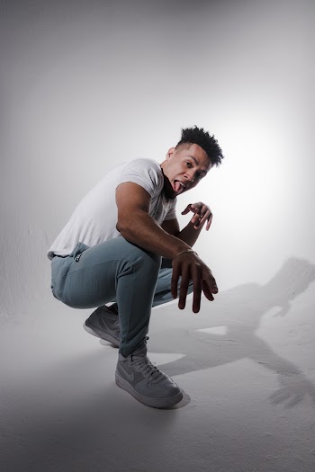 Photo of Man Squat Posing In Front of White Wall Sticking Out His Tongue