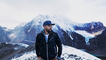 Photo of Man Standing Across Snow Capped Mountains