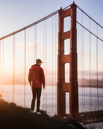 Photo of Man Wearing Jacket Looking at Suspension Bridge