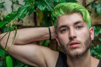 Photo of Man With Green Hair Leaning by the Wall Near Green Plants