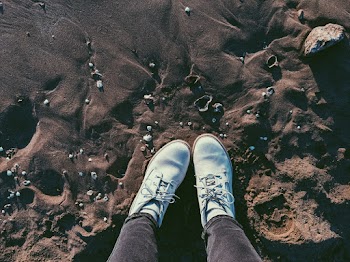 Photo of Person Legs in Boots Standing on Sandy Beach