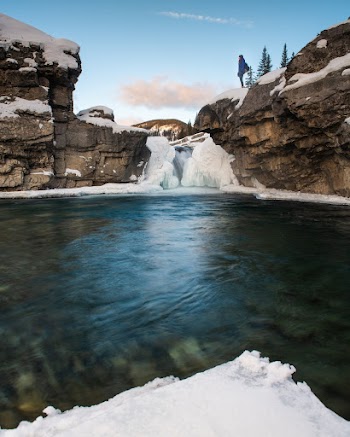 Photo of Person Standing on Rock Formation Near Lake