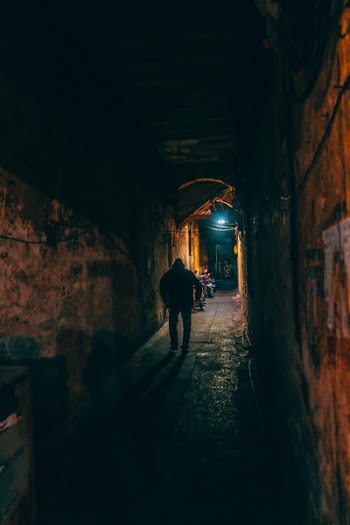 Photo of Person Walking Along Brown Wall Tunnel