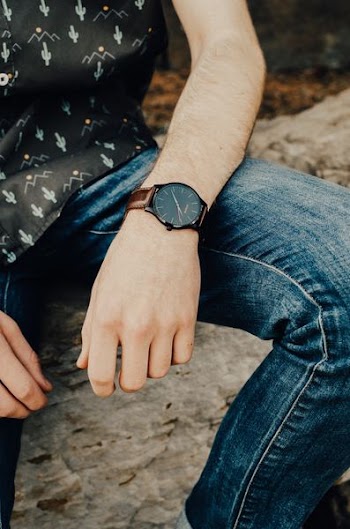 photo of person wearing analog watch and blue jeans and black top