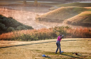Photo of Person Wearing Pink T-shirt and Grey Dress Pants Swinging Golf Club