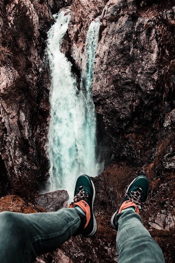 Photo of Person Wearing Sneakers Across Waterfalls