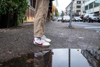 Photo of Person Wearing White and Red Nike Low-top Sneakers Standing Next to a Puddle
