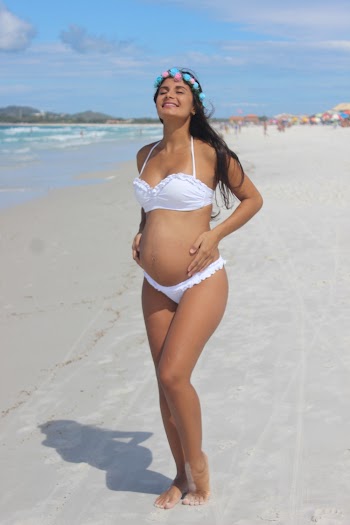 Photo of Pregnant Woman in White Bikini Standing and Smiling on Seashore with Her Eyes Closed