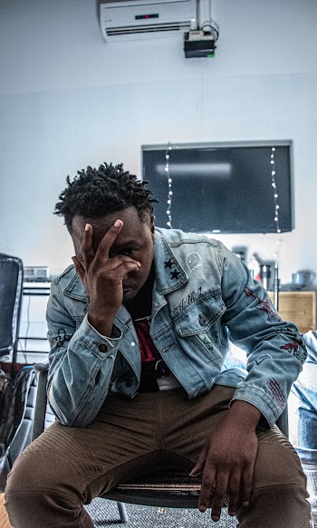 Photo of Sitting Man in Blue Denim Jacket and Brown Pants Posing With His Hands Covering His Face