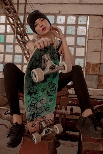 Photo of Sitting Woman in Black Outfit and Black Beanie Posing While Holding Skateboard