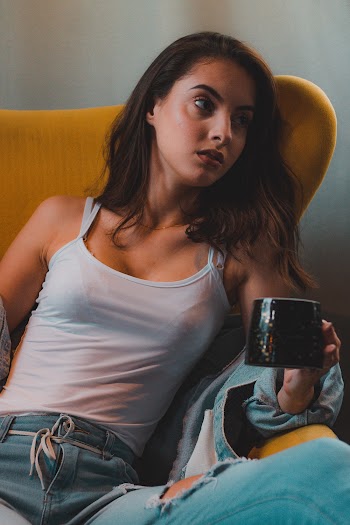 Photo of Sitting Woman in White Tank Top Posing While Holding Coffee Mug
