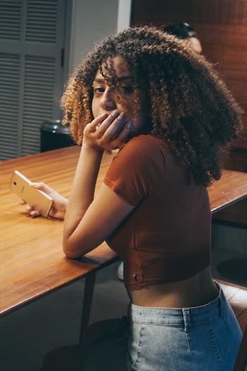 Photo of Sitting Woman Leaning on Table Holding a Smartphone