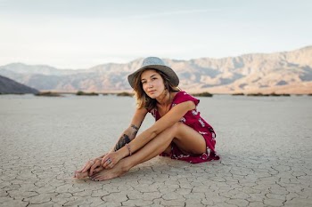 photo of sitting woman wearing red dress and grey cowboy hat with black tattoo in her right arm
